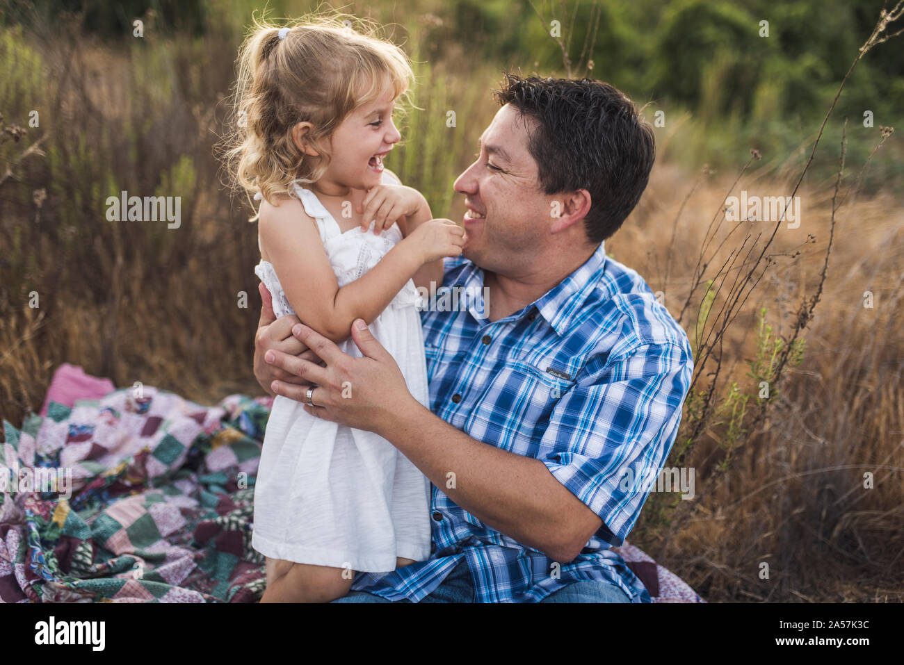 Dad und meinem 4 Jahre alten Tochter lachend im Freien auf Patchwork Quilt Stockfoto