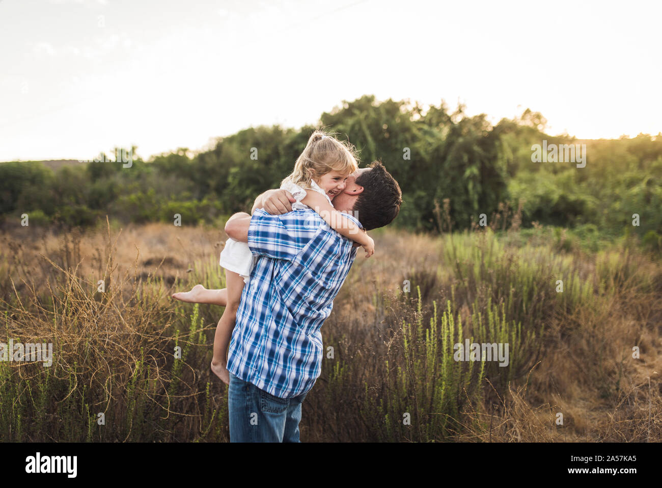 Junge Lachen barfuß Mädchen umarmt Vater draußen im Feld Stockfoto