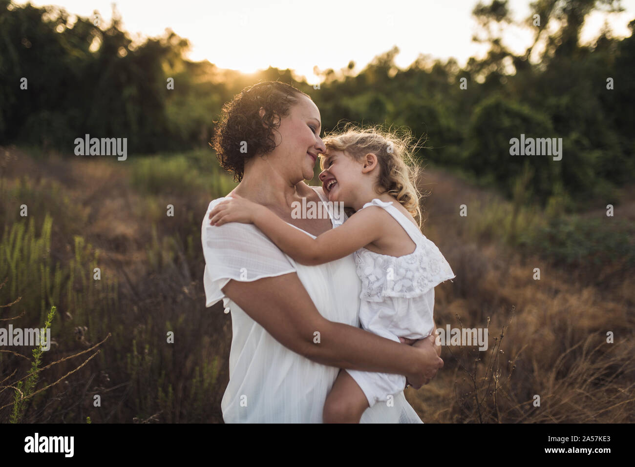 Lächelnde Mutter holding Lachen 4 Jahre alten Tochter an einem sonnigen Feld Stockfoto