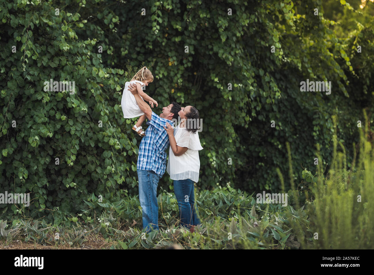 Vati hält junge Tochter in Luft als Mama lächeln über seine Schultern Stockfoto