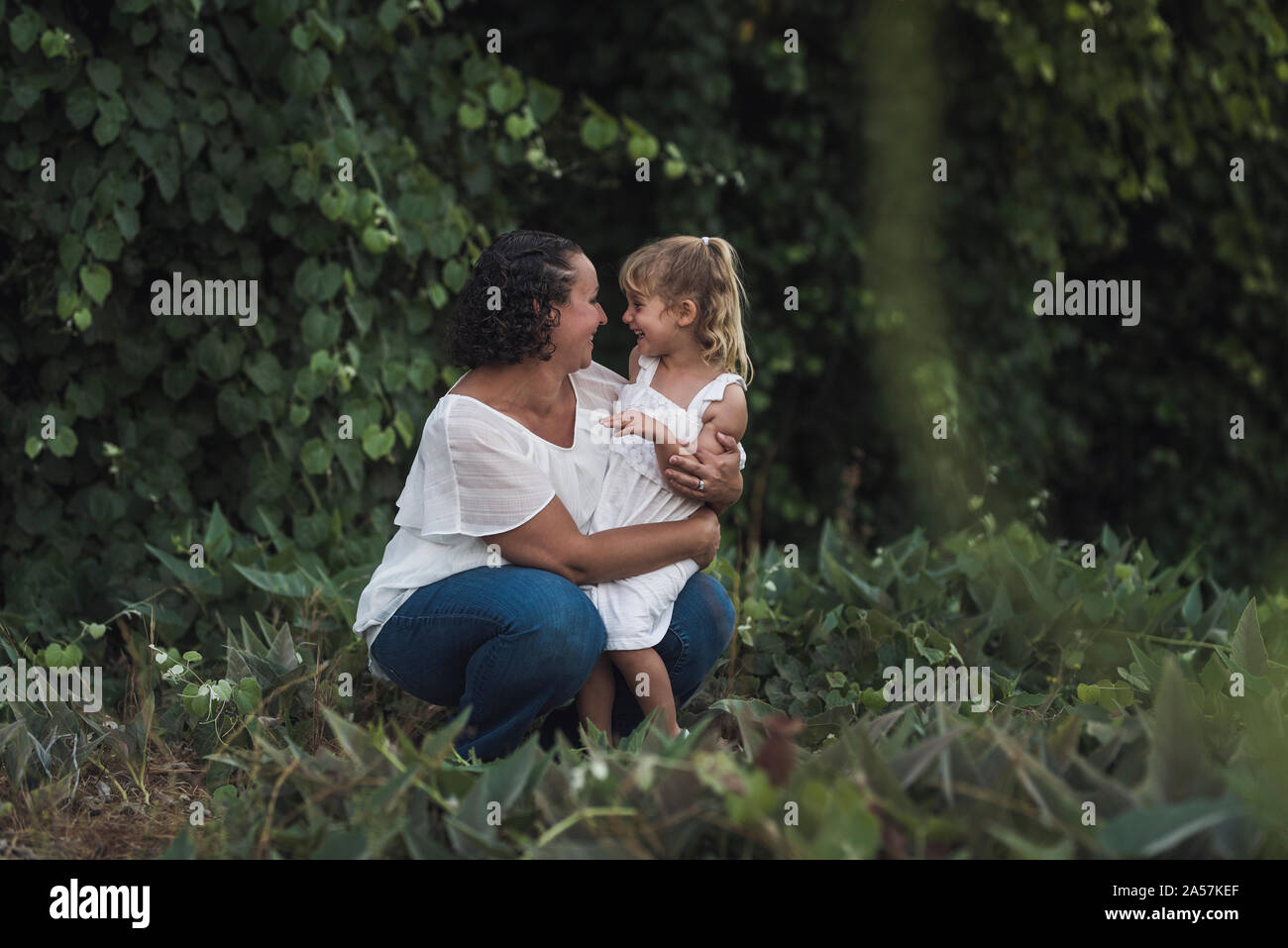 Lachend mom Knieten zu umarmen, 4 Jahre alte Tochter in der Nähe von üppiger Pflanzen Stockfoto
