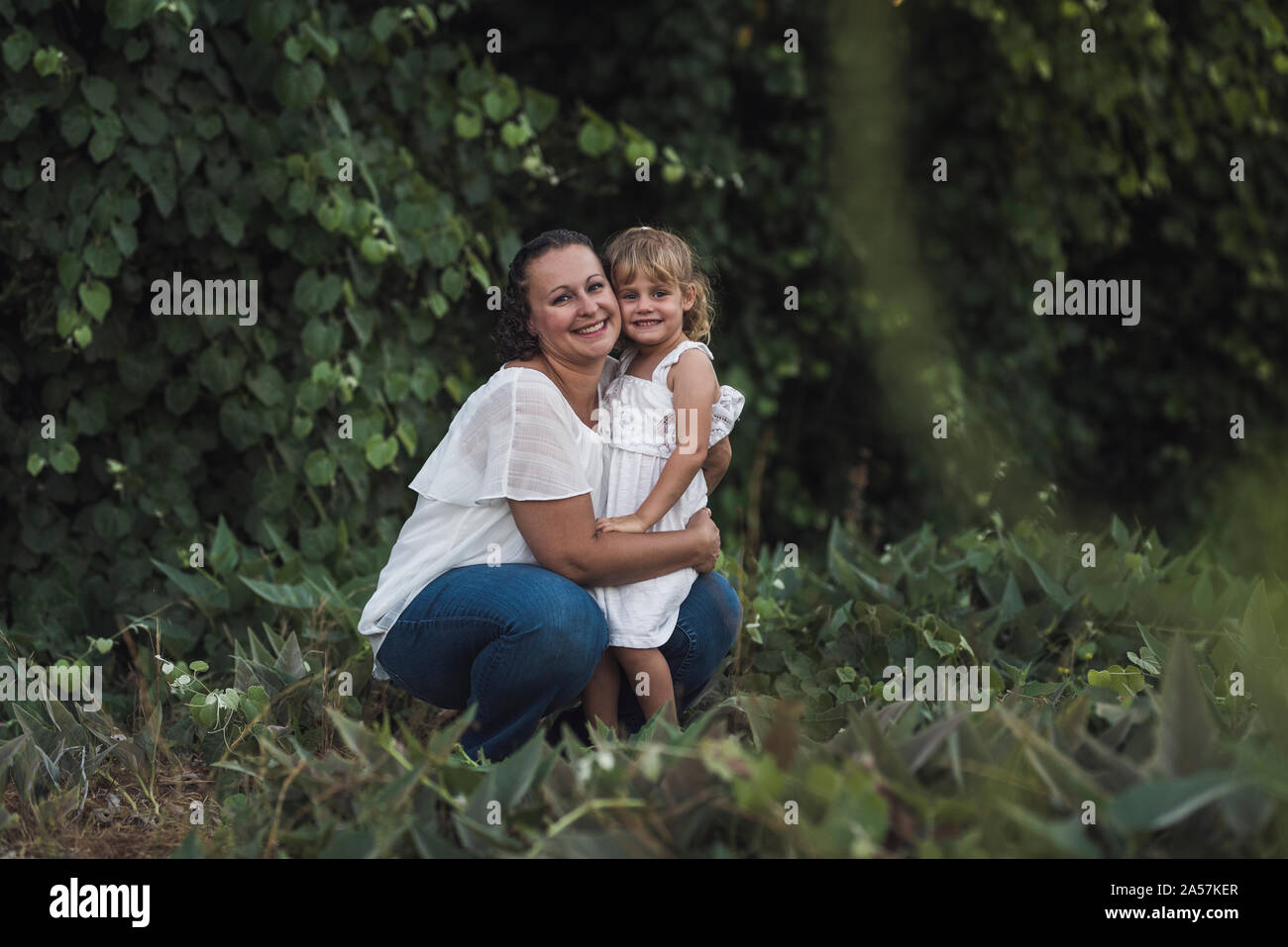 Kniend Mutter umarmt glücklich Tochter im Freien in der Nähe von Tree Stockfoto