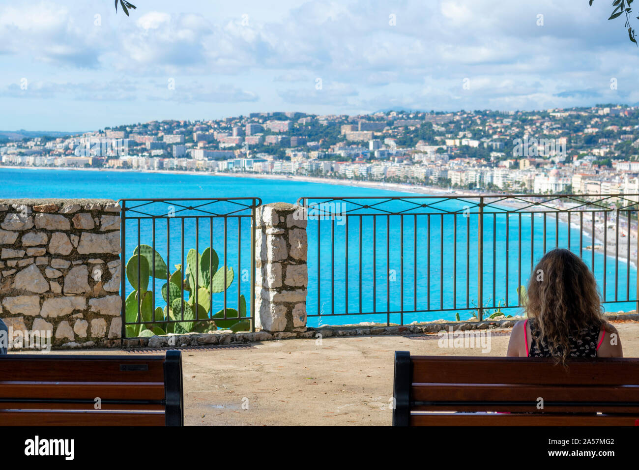 Eine Frau sitzt auf einer Bank von einem Aussichtspunkt an der Burg mit Blick auf das Mittelmeer, die Bucht der Engel, der Strand und die Stadt Nizza, Frankreich. Stockfoto