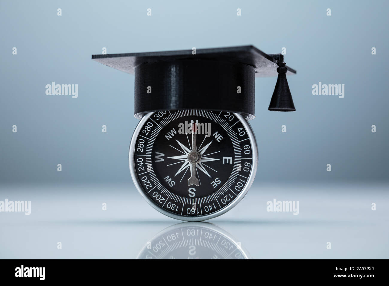 Skalenhaube auf Kompass auf grauen Hintergrund. Hochschule Wahl Konzept Stockfoto
