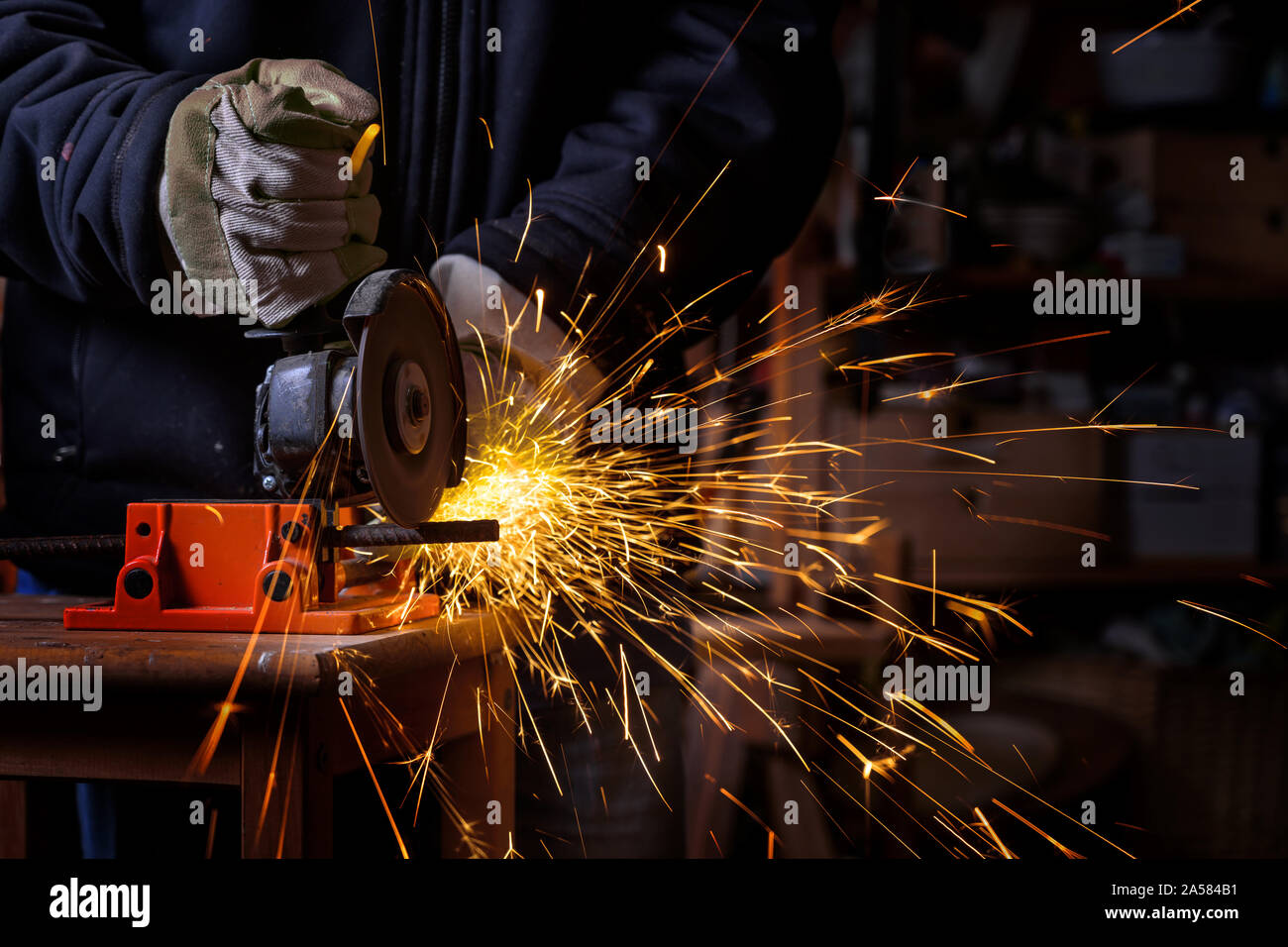Die Hände eines Handwerkers mit Arbeitshandschuhen Schneiden eine Eisenstange mit dem elektrischen Winkelschleifer die Sprays viele heiße in der dunklen Werkstatt Funken, Gefahr Stockfoto