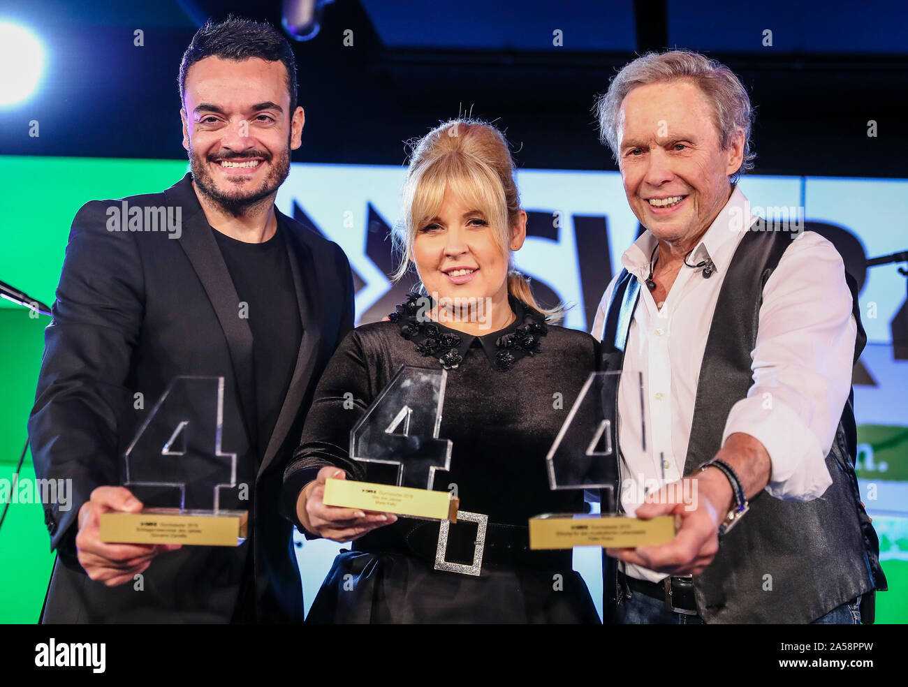 Stuttgart, Deutschland. Okt, 2019 18. Die pop Sänger Giovanni Zarrella (L-R), Maite Kelly und Peter Kraus präsentieren ihre Preise bei der SWR4 Veranstaltung 'gläsernen Vier'. Zarrella ist "Newcomer des Jahres", Kelly "Star des Jahres" und Kraus erhielt den Preis für sein musikalisches Leben. Credit: Christoph Schmidt/dpa/Alamy leben Nachrichten Stockfoto