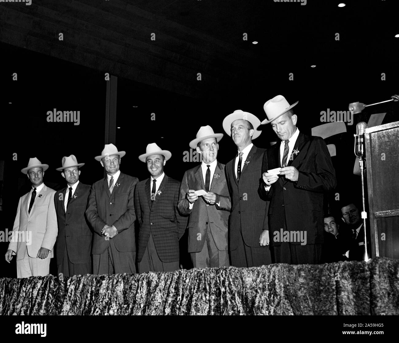 (4 Juli 1962) - - - Die ursprünglichen sieben Mercury Astronauten, jedem tragen Neue cowboyhüte und ein Abzeichen in der Form eines Sterns, abgebildet auf der Bühne an der Sam Houston Coliseum. Eine große Menschenmenge war an Hand sie zu Houston, Texas begrüßen zu dürfen. Zu recht sind Astronauten M. Scott Carpenter, L. Gordon Cooper jr., John Glenn Jr., Virgil Grissom, Walter I. M. Schirra jr., Alan B. Shepard, Jr., und Donald K. Slayton verlassen. Senator John Tower (R-Texas) ist ganz rechts im Hintergrund zu sehen. Stockfoto