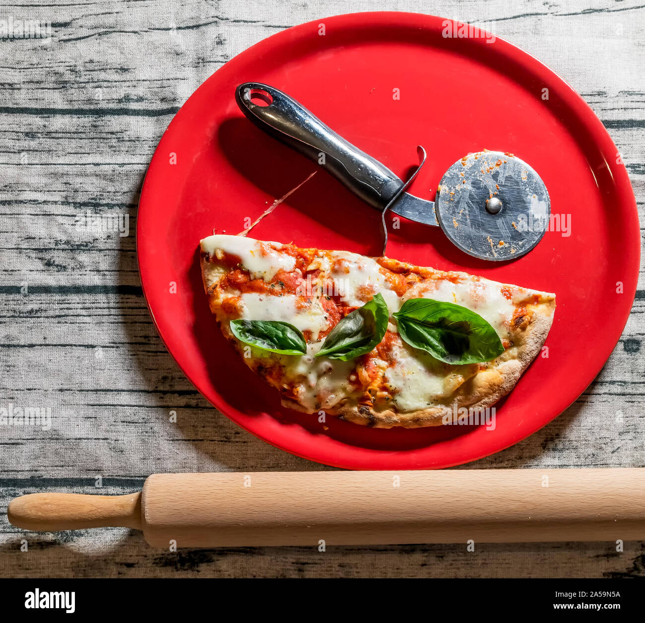 Typisch italienische Pizza in der Hälfte mit der speziellen Rad in ein rotes Schild mit einem hölzernen Rolling Pin daneben Stockfoto