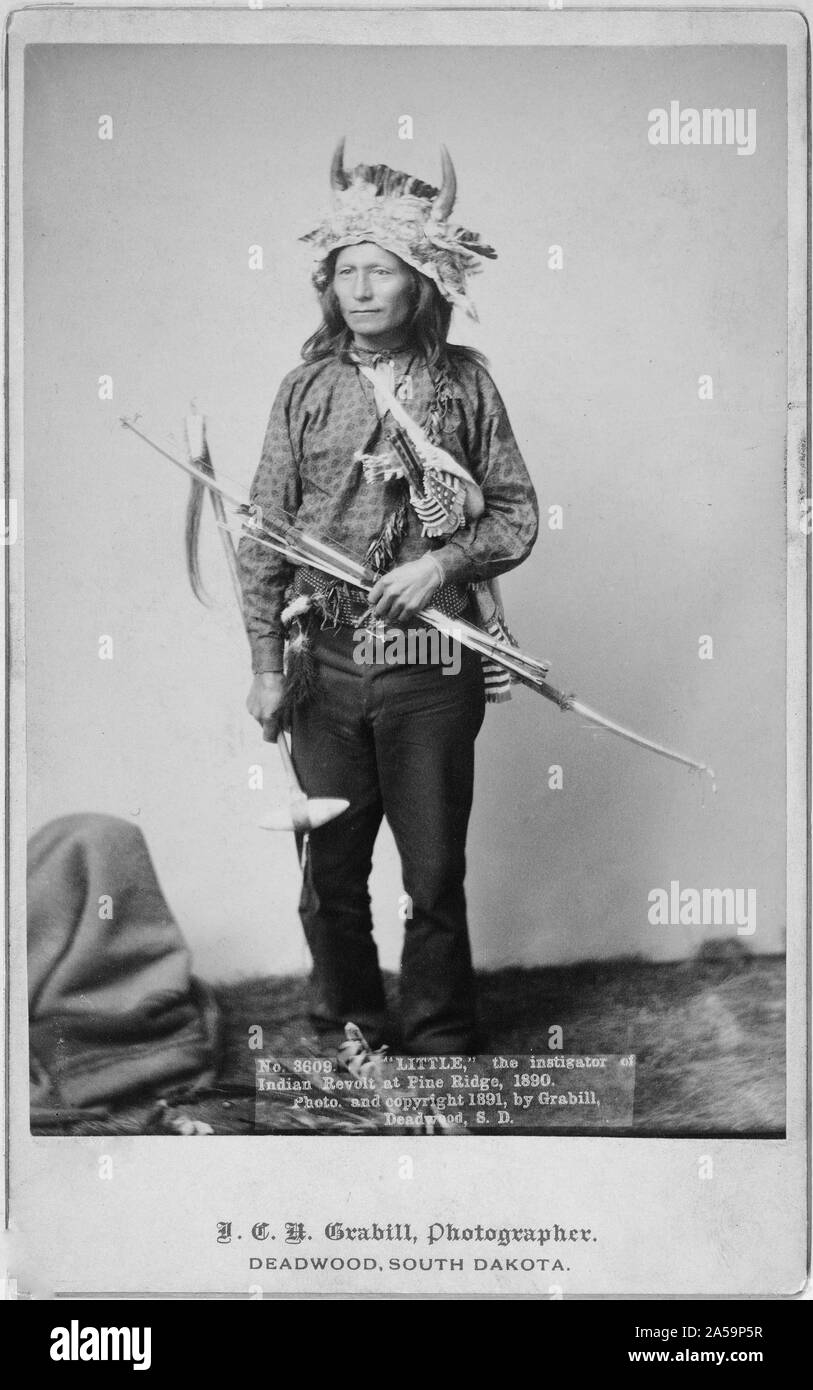 Wenig, Oglala Band Leader, full-length Studio Portrait, stehend, nach vorne, das Tragen von Horn Kopfschmuck, Hose und Shirt, und halten Bogen, Pfeile und Tomahawk. Stockfoto