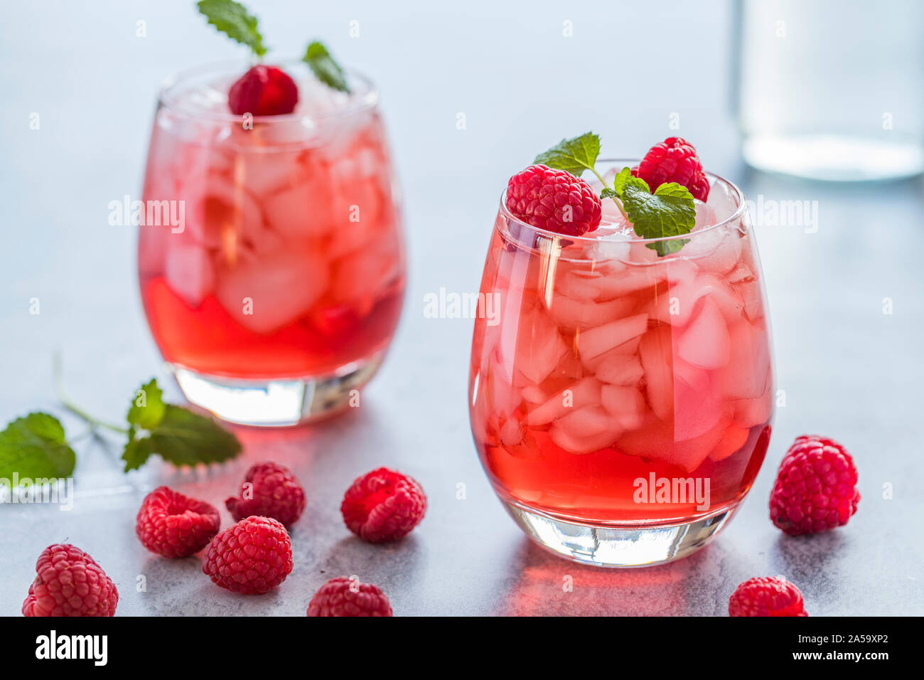 Zwei frischen Rot transluzent Getränke mit Ice und Himbeeren. Die himbeersaft ist mit einem grünen Blatt garniert, und es gibt stücke, die von Eis und Ra Stockfoto