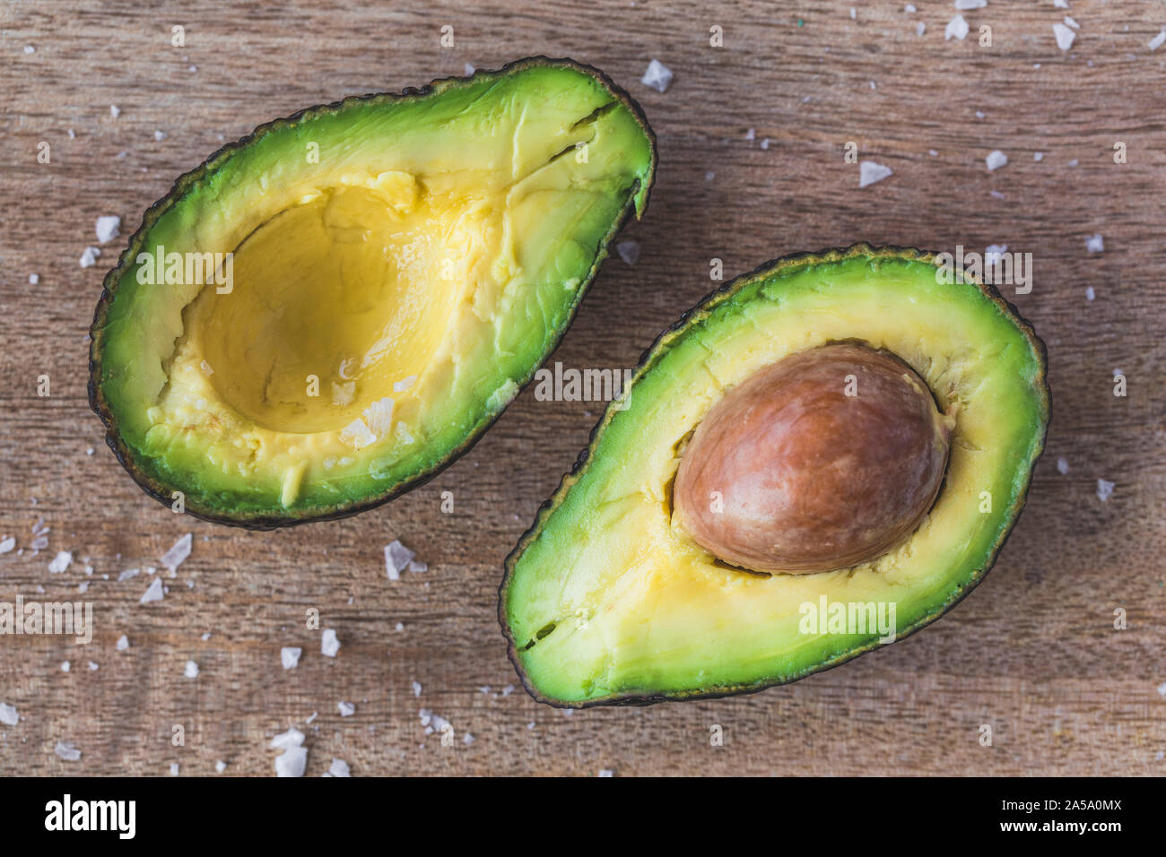 Eine Avocado in zwei mit der Grube in einem der Früchte Hälften aufgeteilt, und einige Meersalz auf dem Holztisch. Die Kamera wird direkt von oben, flach Stockfoto