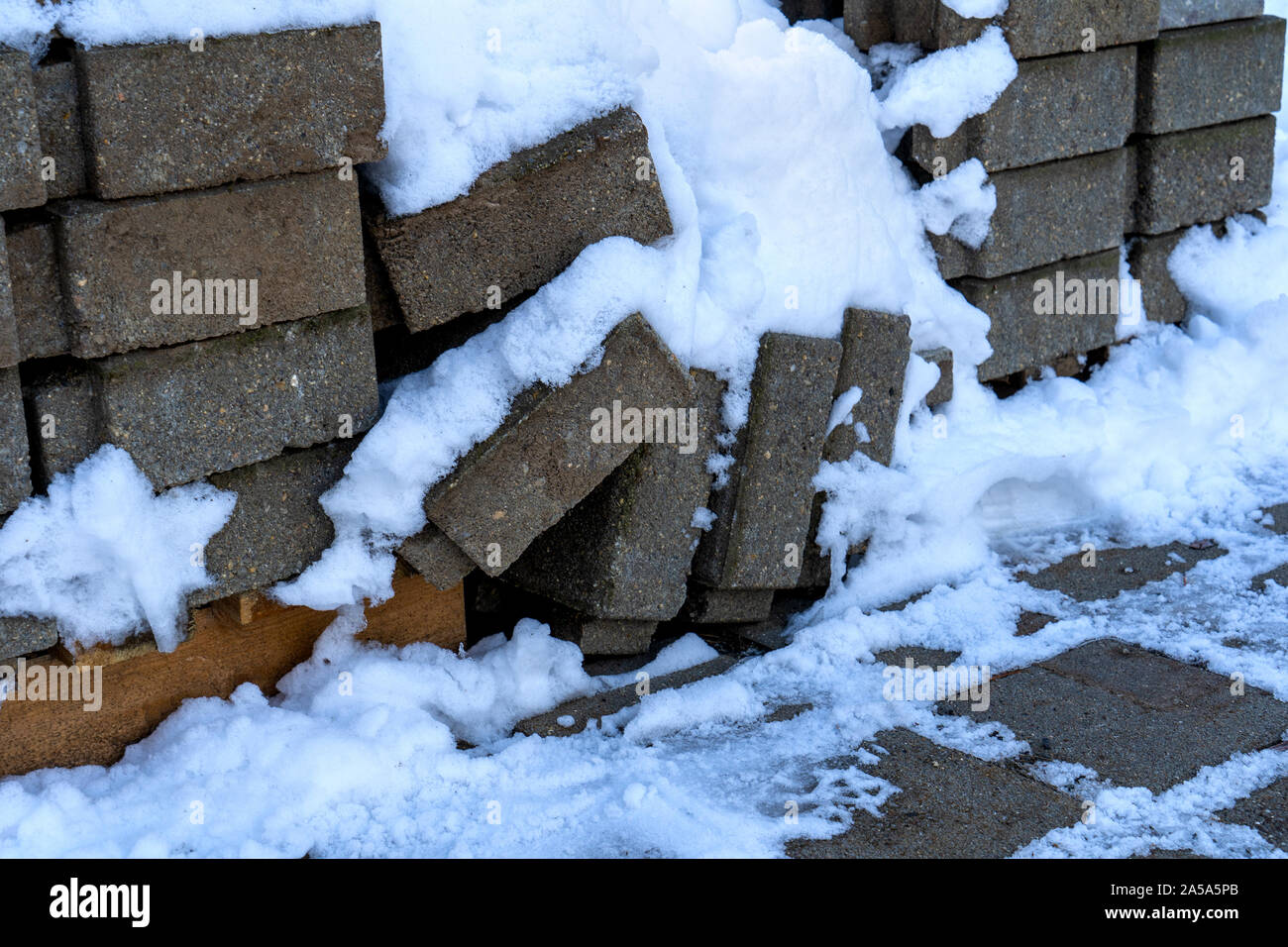 Pflastersteine warten im Winter verwendet werden. Sie sind unter Schnee bedeckt. Einige der Steine fielen von dem Haufen. Stockfoto