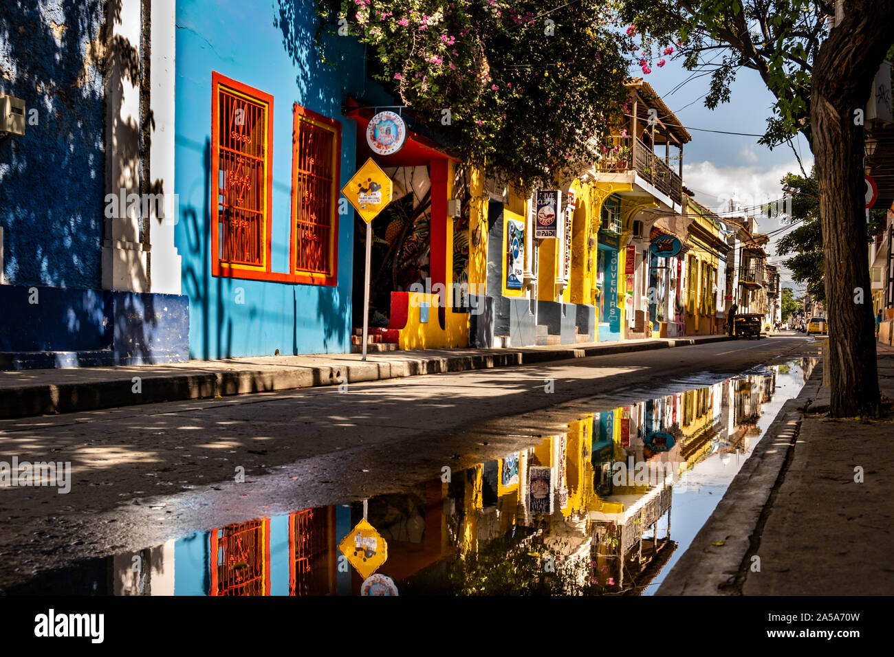 Farbenfrohe Gebäude in einer großen Pfütze, in einer ruhigen Seitenstraße in der Altstadt von Santa Marta in Kolumbien zum Ausdruck Stockfoto
