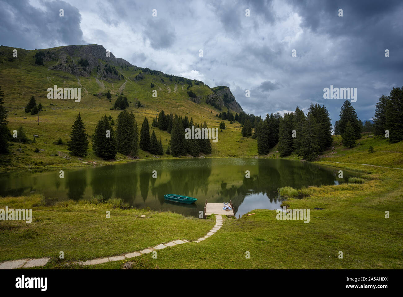 Mountain Lake mit einem Mann lag auf dem Rücken auf einem Steg mit einem gebundenen Ruderboot Stockfoto