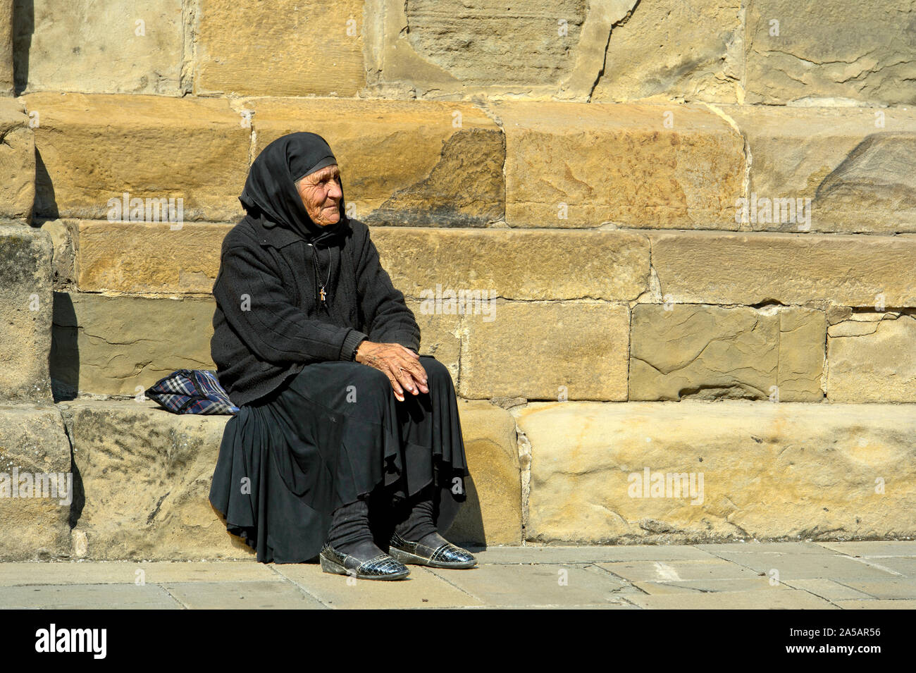 Alte georgische Frau in schwarzem Kleid auf einem Stein am Svetitskhoveli Kathedrale, Mtskheta, Georgien sitzen Stockfoto