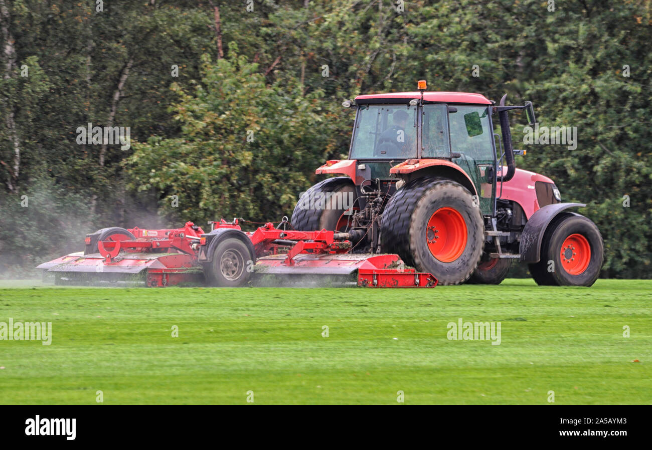 Traktor mit Anhänger Mähen von Gras mit Wasser spritzen in der Luft Stockfoto