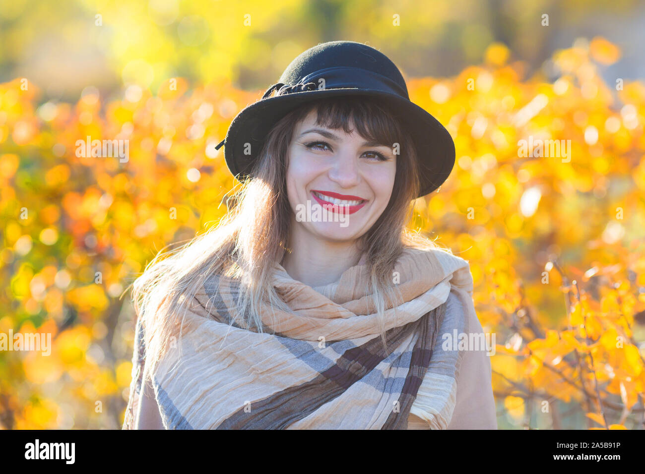 Eine hübsche Frau von 30-35 Jahre alt mit einem schönen Lächeln in einem Hut und Mantel in der Nähe von einem gelben Bush. Stockfoto
