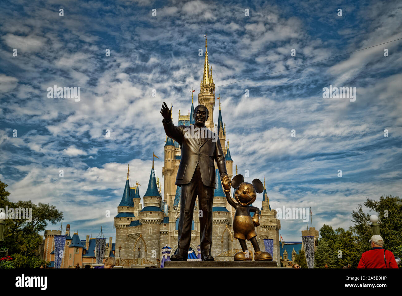 Cinderellas Schloss im Magic Kingdom mit der Walt Disney und Mickey Statue im Vordergrund und Wolken am Himmel im Hintergrund, Orlando, Florida Stockfoto