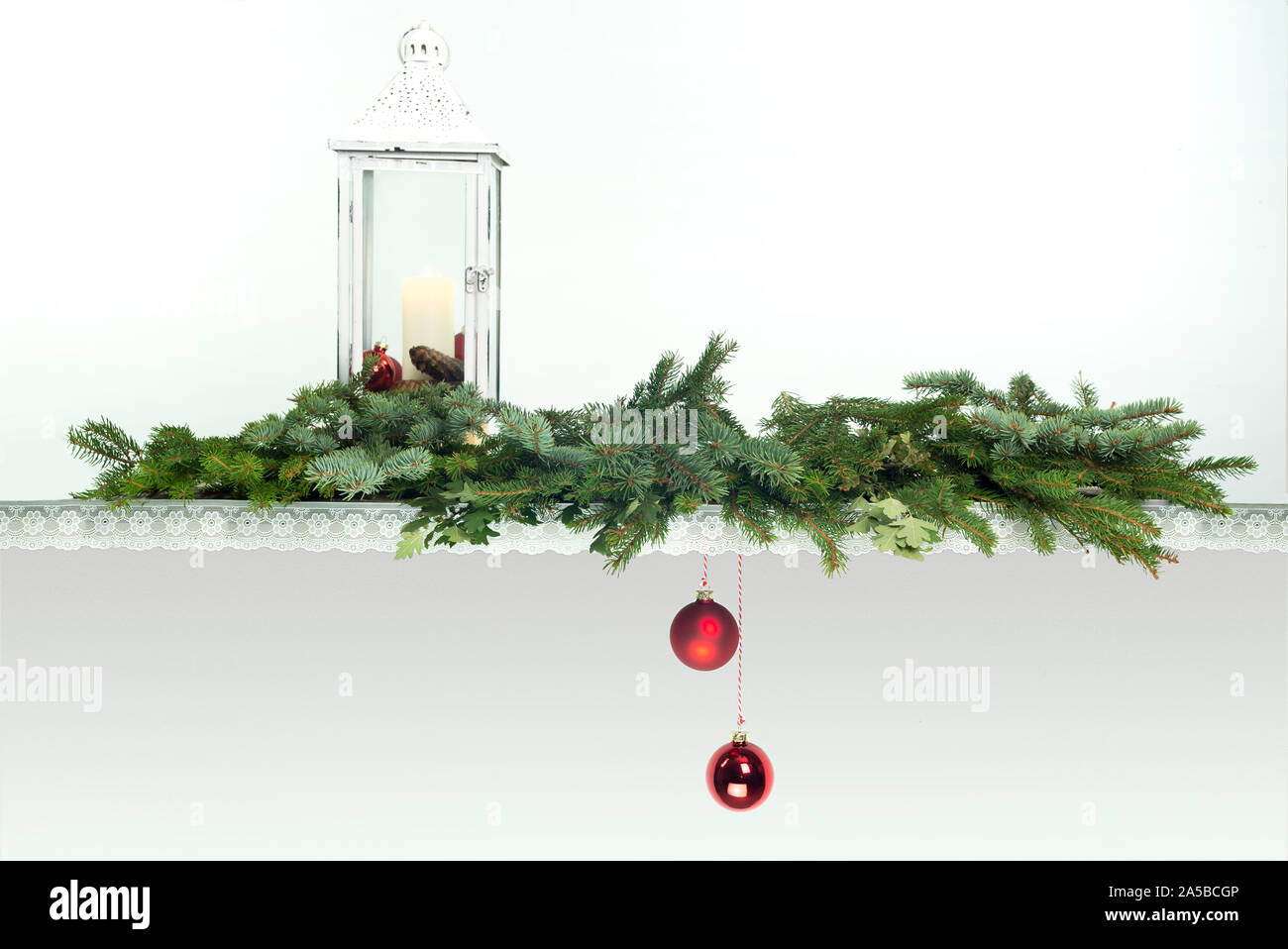 Ein altes Holzbrett mit Spitze verziert. Vintage Laterne mit Kerze. Zweige der Tannen Blau und Grün. 2 rote Weihnachtskugeln sind nach unten hängen. Stockfoto