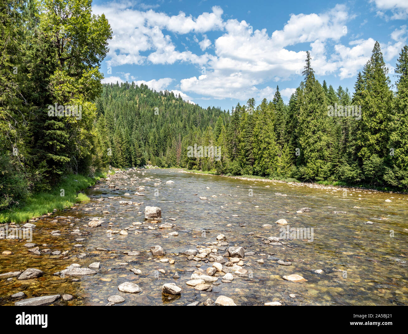 Mountain Stream über felsige Flussbett mit Bäumen und blauen Himmel im Hintergrund fließt. Stockfoto