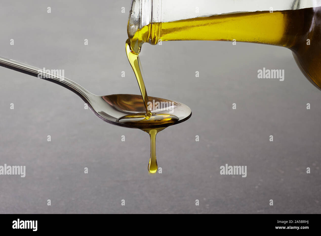Gießen Olivenöl aus Glas Flasche auf grauem Hintergrund Stockfoto