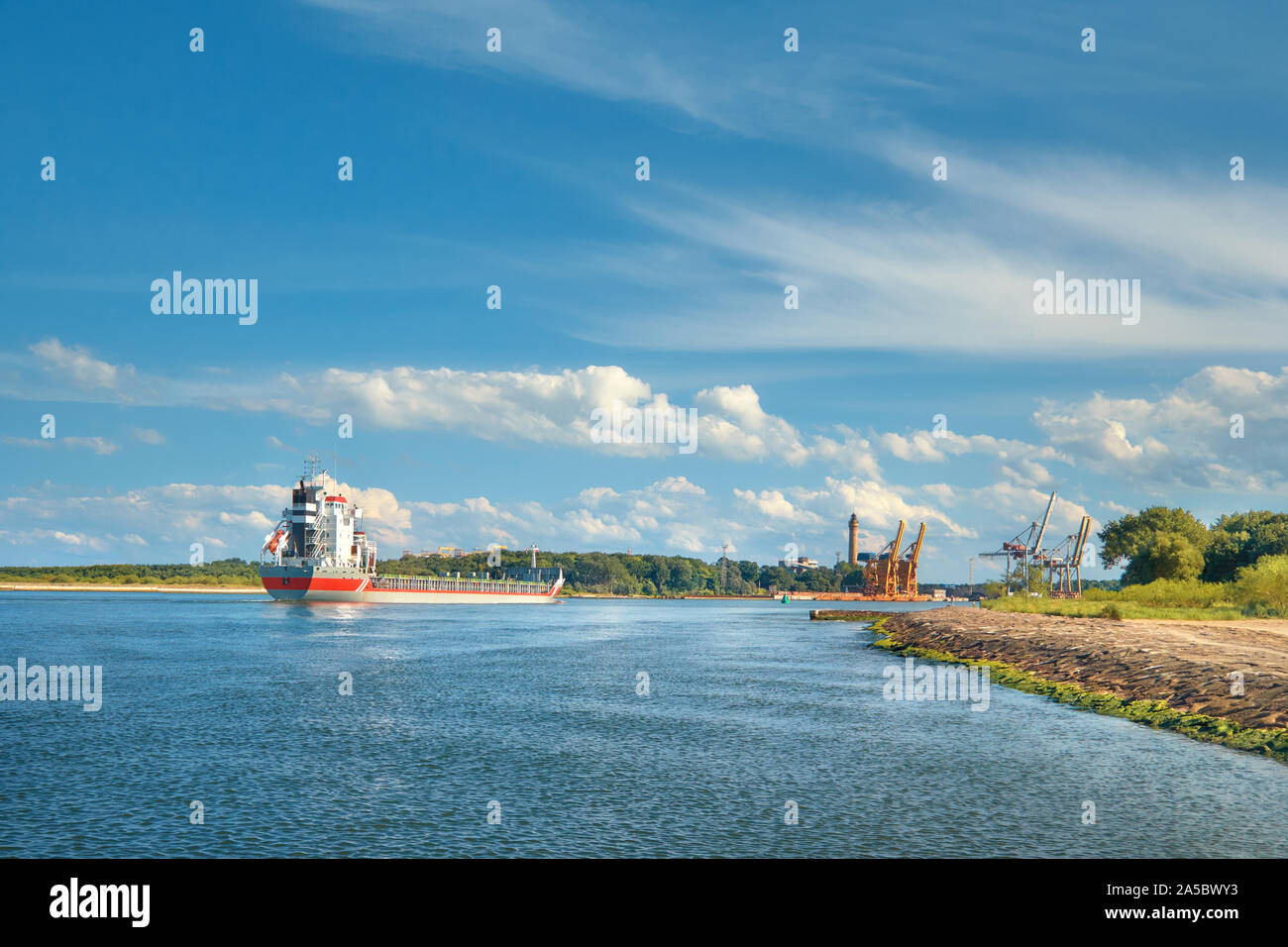 Große Container Cargo Schiff Die Häfen Swinoujscie, Polen, an einem sonnigen Tag mit blauem Himmel und Wolken Stockfoto