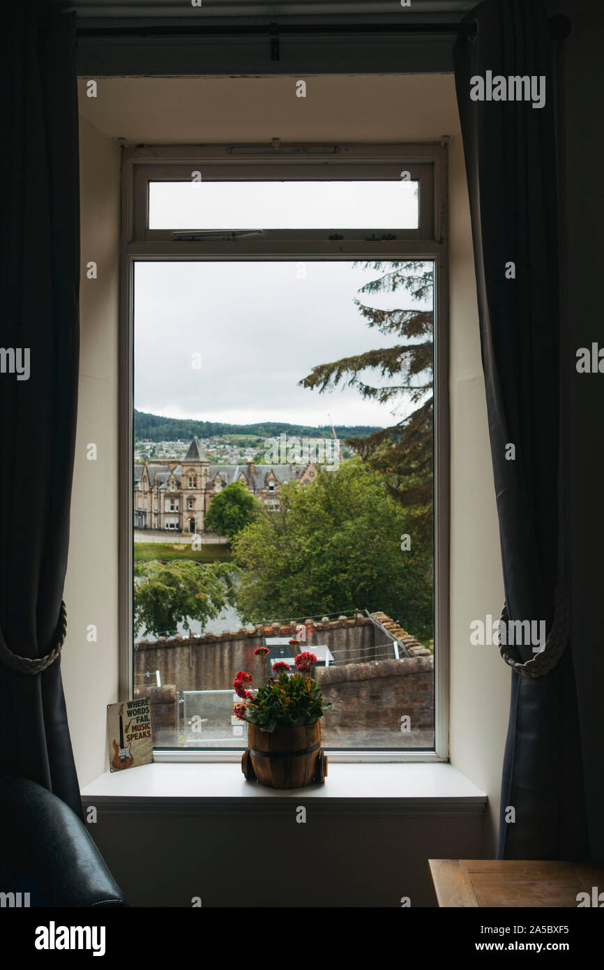 Sie suchen ein Hotel in Inverness, Schottland. Eine Topfpflanze sitzt auf der Fensterbank, während Gebäude aus den 1870er Jahren im Hintergrund sichtbar sind Stockfoto