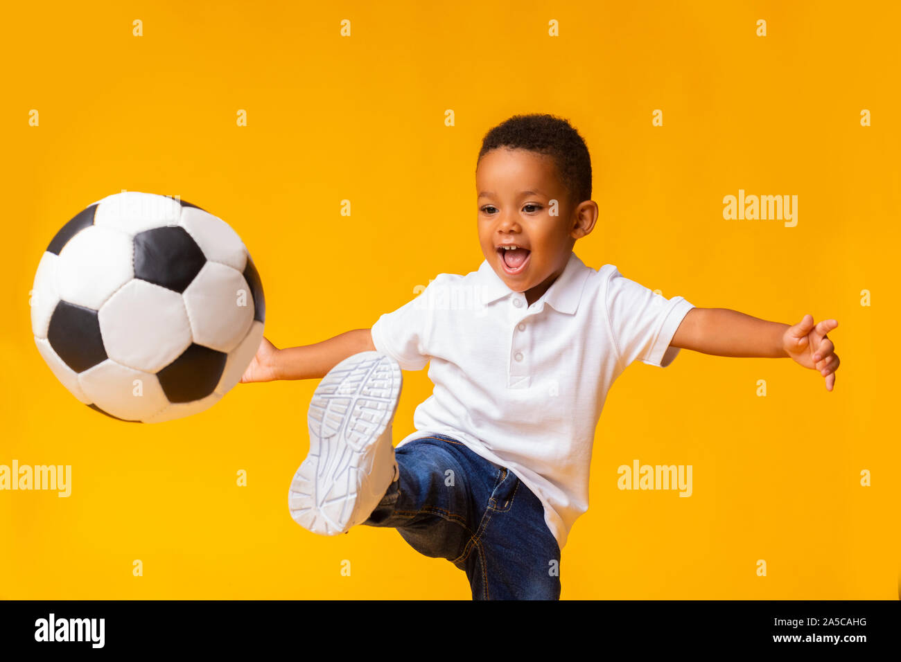 Adorable kleinen Jungen Fußball spielen, schlagen Kugel über gelben Hintergrund Stockfoto