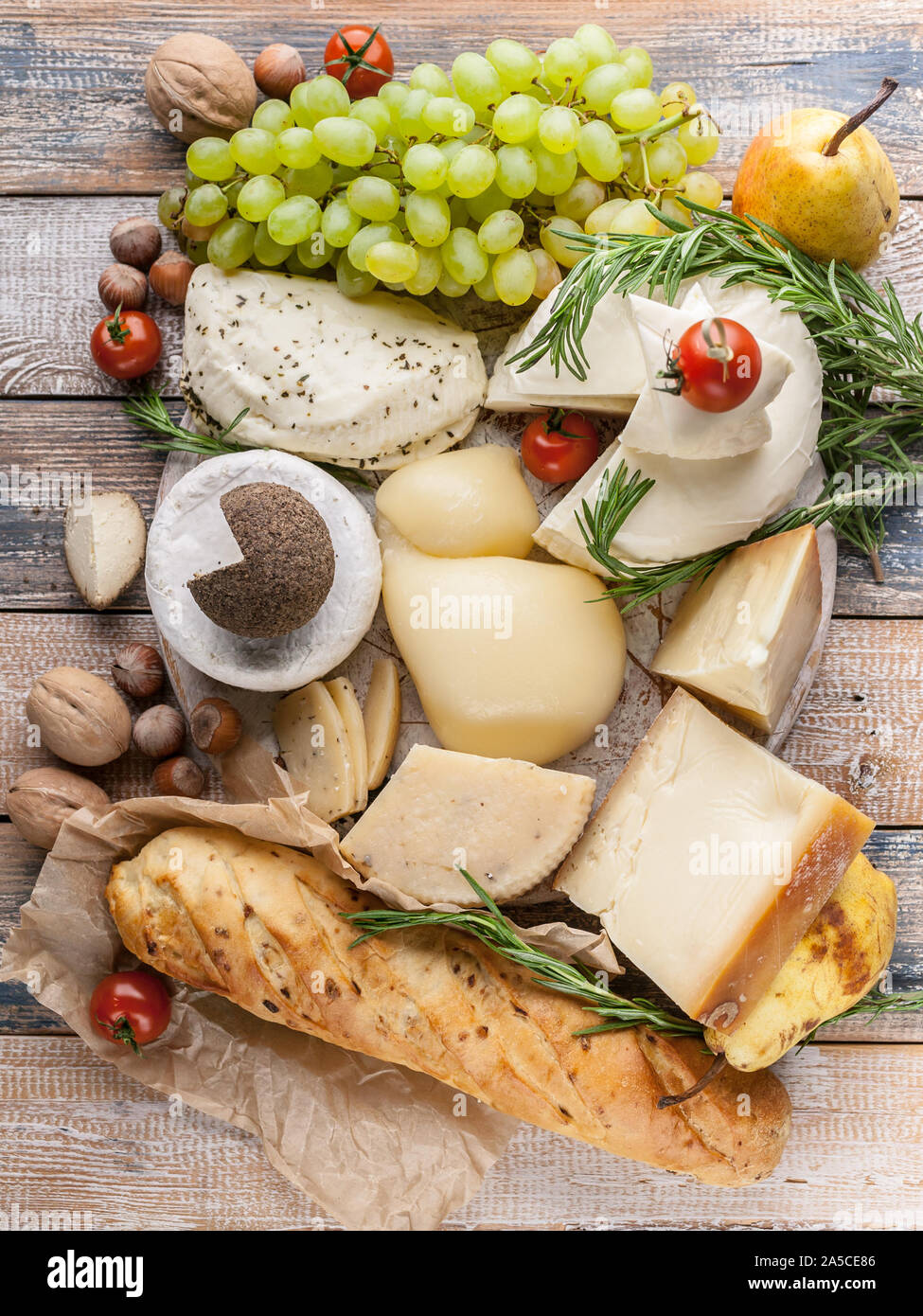 Ansicht von oben verschiedene köstliche Käsesorten, Nüsse, Früchte, würzige Kräuter und Zwiebeln baguette auf einem urigen Hintergrund. Vertikaler Dampfstoß Stockfoto