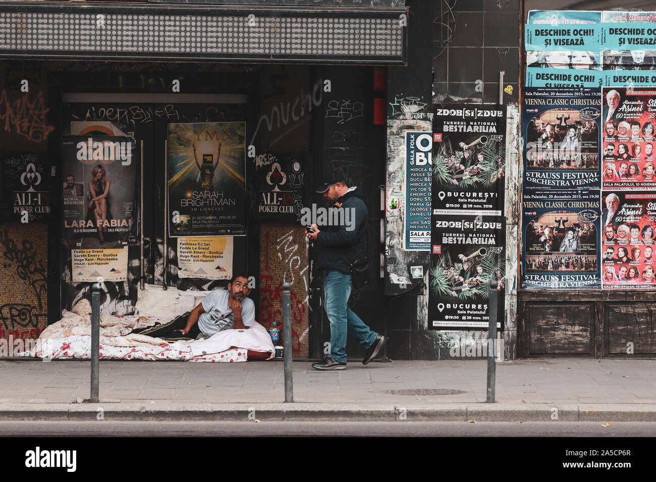 Bukarest, Rumänien - Oktober 19, 2019: Obdachloser auf dem Bürgersteig, die auf einer Matte neben einem verlassenen Gebäude, mit Menschen in Downt Stockfoto