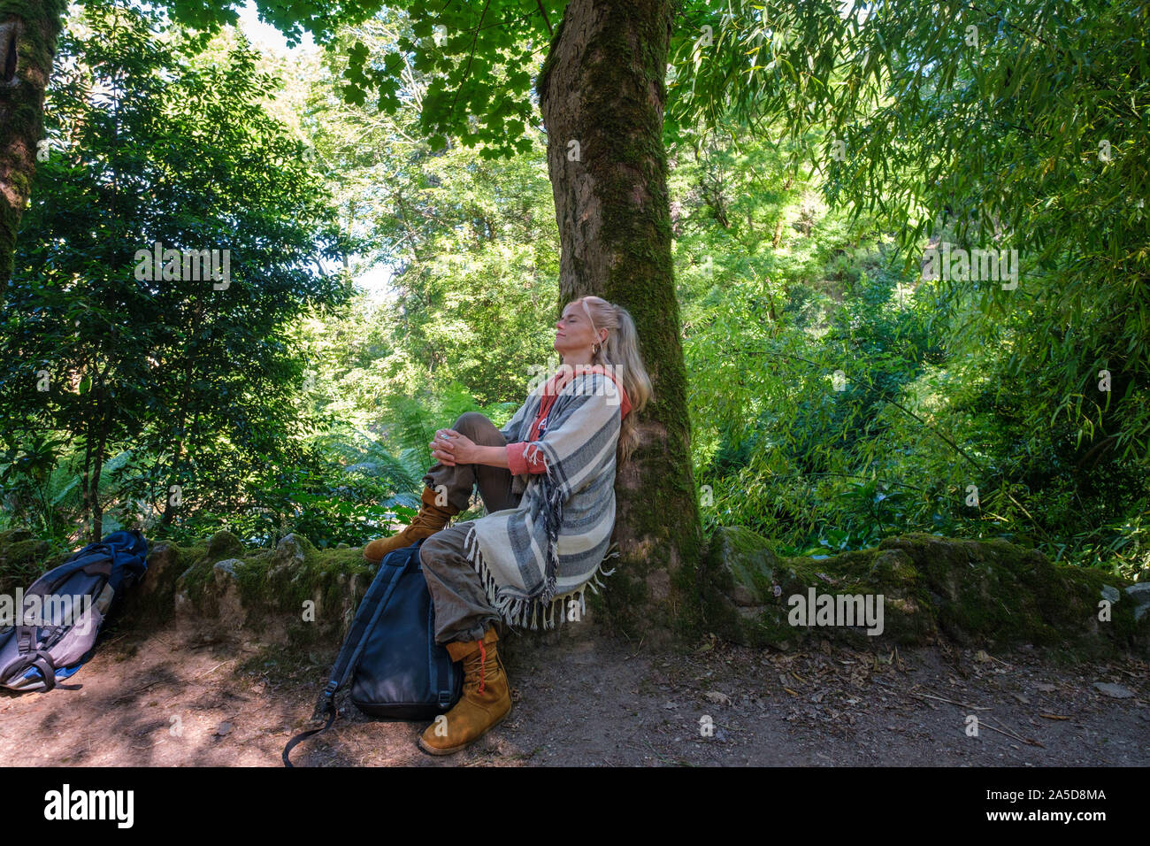 Blonde Frau sitzt neben einem Baum mit den Augen bei einem Wald baden Sitzung geschlossen Stockfoto