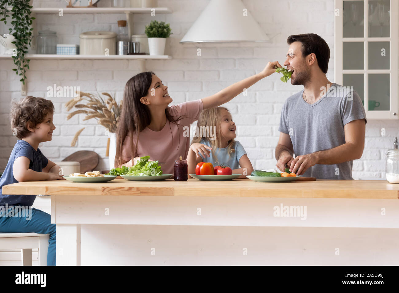 Glückliche Familie kochen Salat zusammen, lächelnde Mutter Fütterung Vater Stockfoto