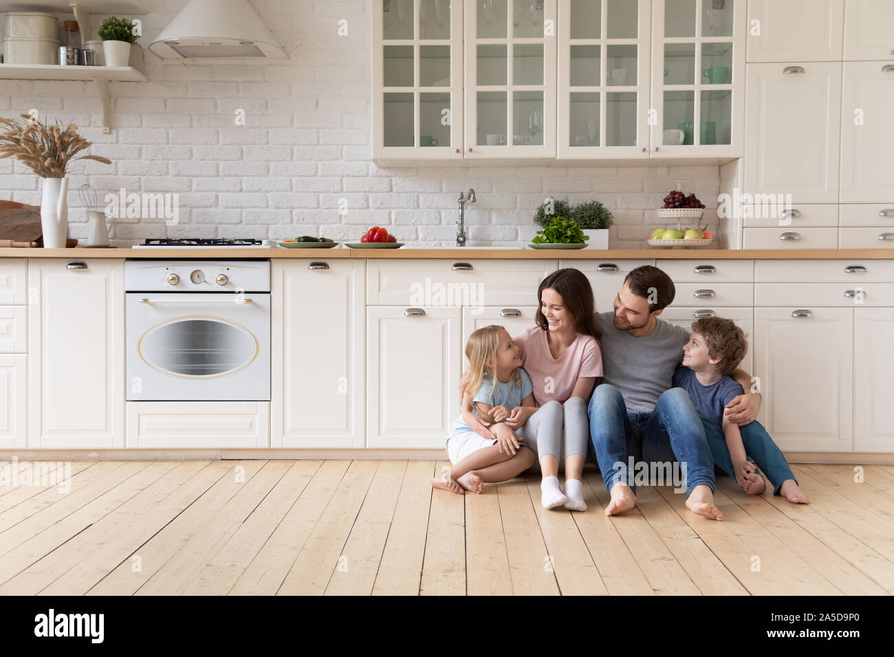 Glückliche Familie mit Kinder sitzen auf dem Boden in der modernen Küche Stockfoto