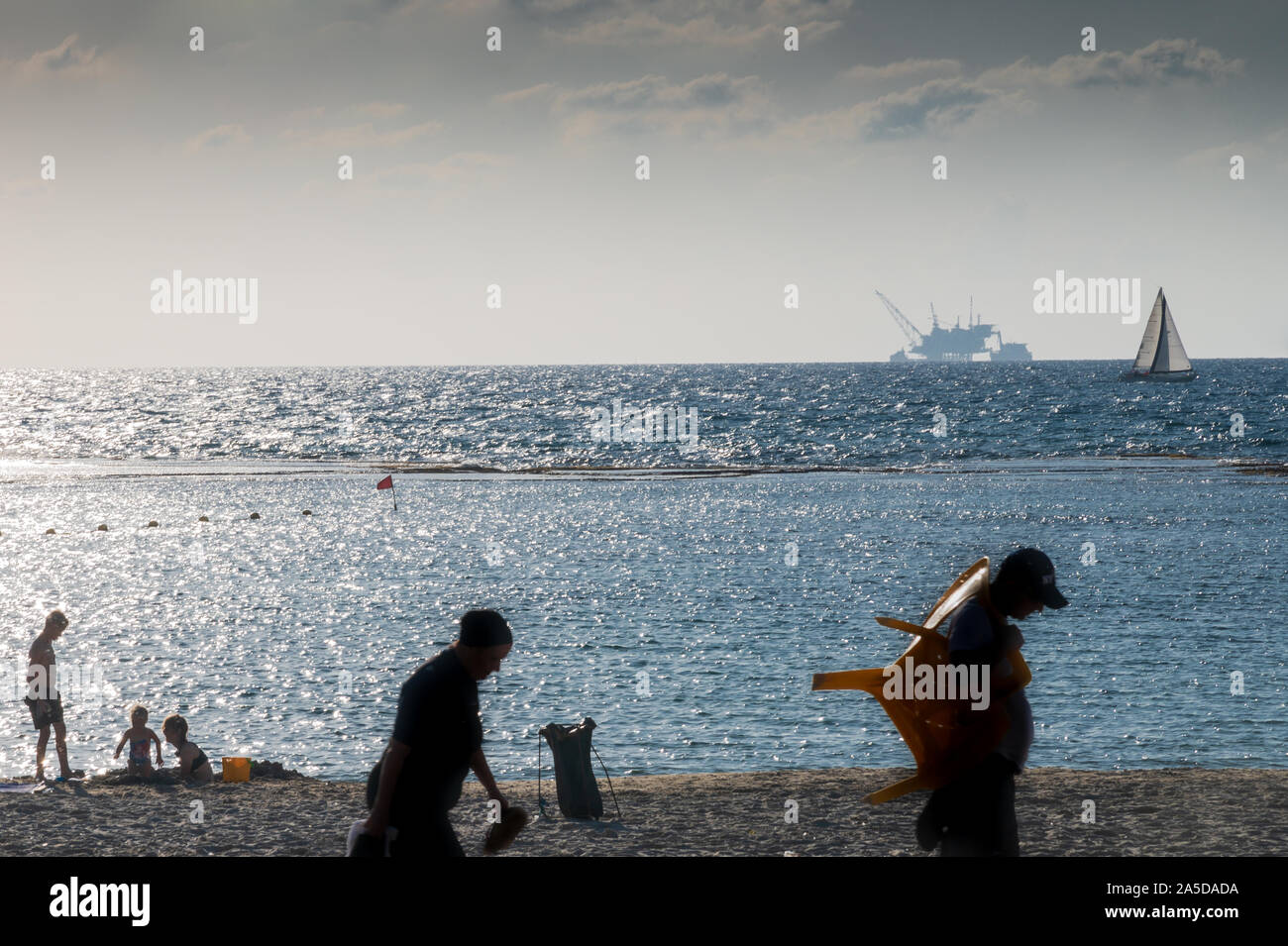 DOR STRAND, Israel/18 OKT 2019: Badegäste am Strand als Segelboot an der Vorderseite der ökologisch umstrittene offshore Bohrinsel Stockfoto