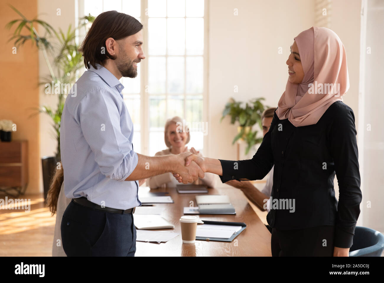 Gerne asiatische muslimische Mitarbeiterin erhalten gefördert Handshake kaukasischen Boss Stockfoto