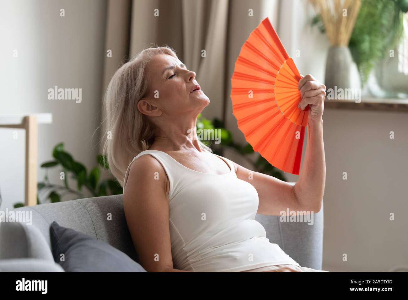 Betonte alte Frau winkte Ventilator leiden vor Überhitzung zu Hause Stockfoto