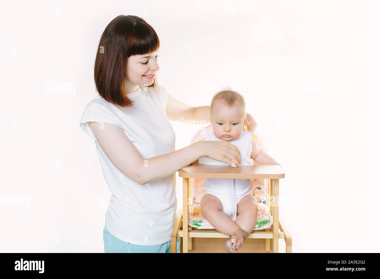 Junge schöne Mutter stellt ein weißes Lätzchen auf ihrem Baby Mädchen, sitzend auf einem Stuhl Stockfoto