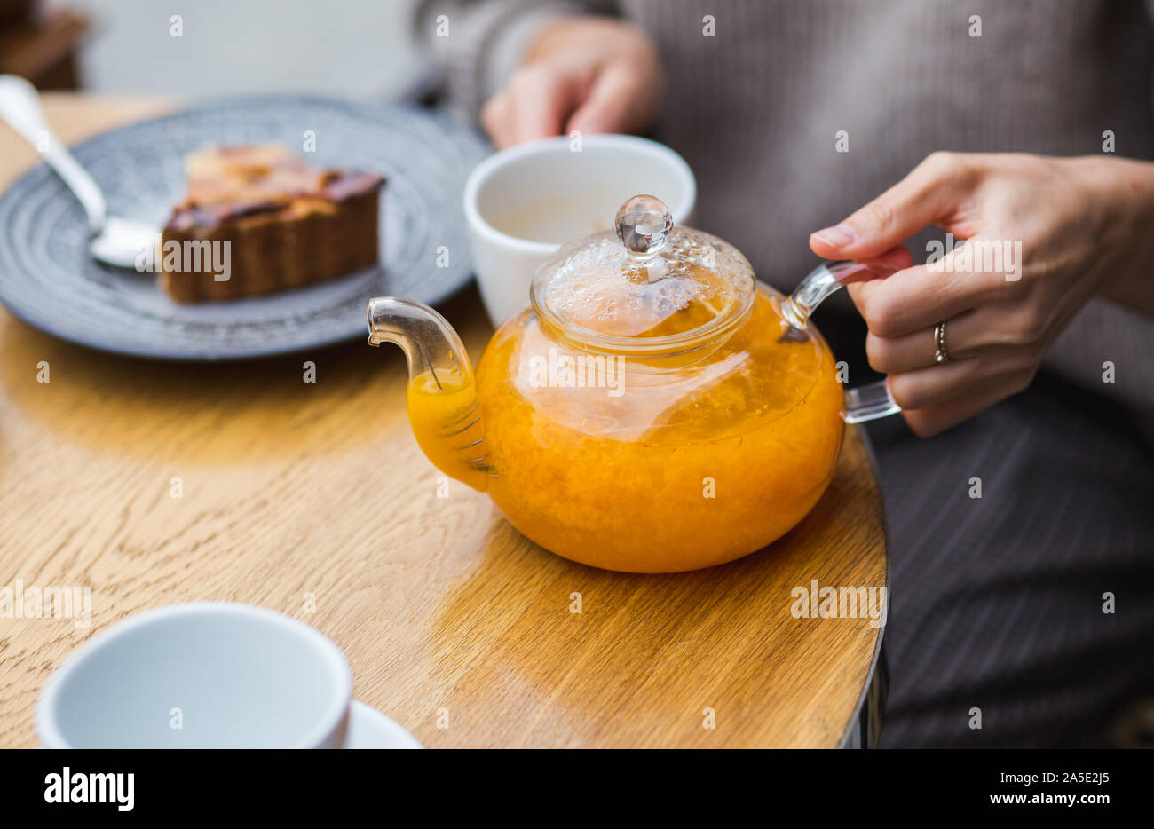 Mädchen gießt aus einem pflanzlichen Berry Tee von Teekanne aus Glas in die Kappe auf hölzernen Tisch Hintergrund. Cafe in der Straße. Stockfoto