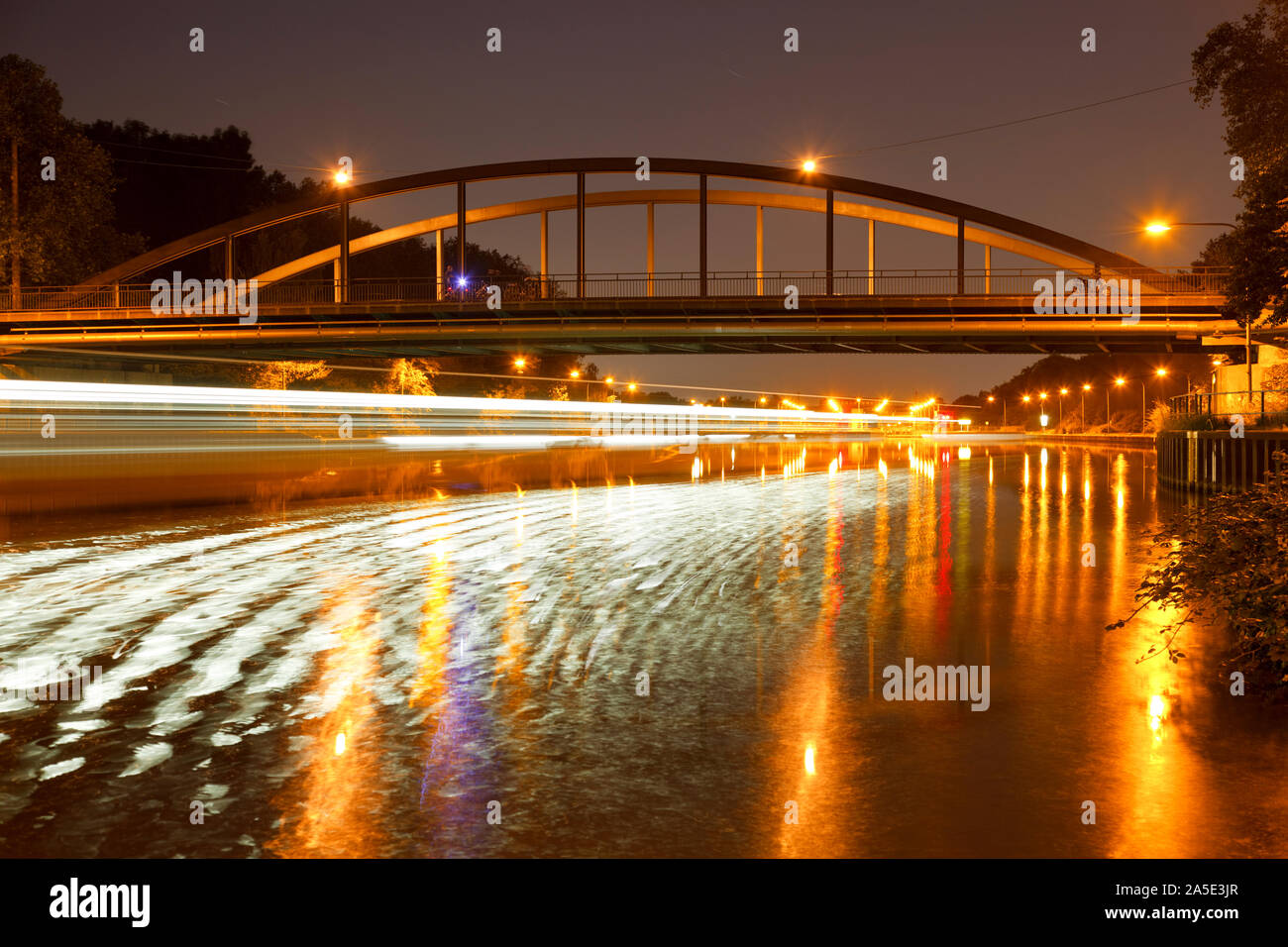 Night Shot mit einem Schiffe licht Trail und Reflexion vor einer Brücke kurz vor der Schleuse. Stockfoto