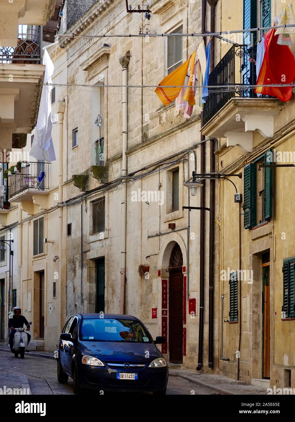 Motorrad- und Autofahrt auf der schmalen Straße mit überhändigen bunten Bettlaken, Wäscherei, Matera, Basilikata, Italien. Stockfoto