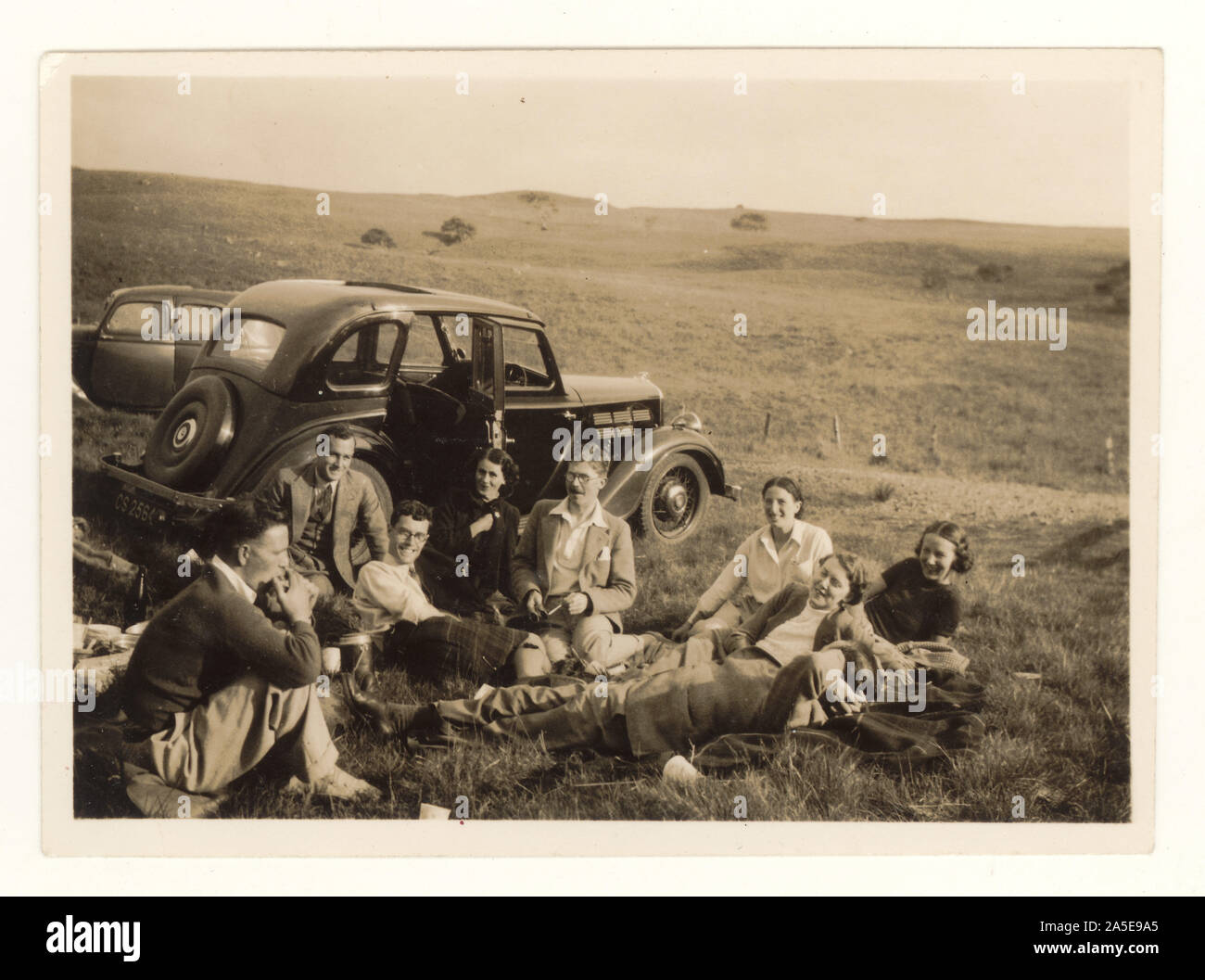 Foto aus dem frühen 20. Jahrhundert von einer Gruppe von Freunden, die ein Picknick neben einem Oldtimer machen, in Moorlandschaft, ca. Mitte der 30er Jahre, Ayrshire, Schottland, Großbritannien Stockfoto