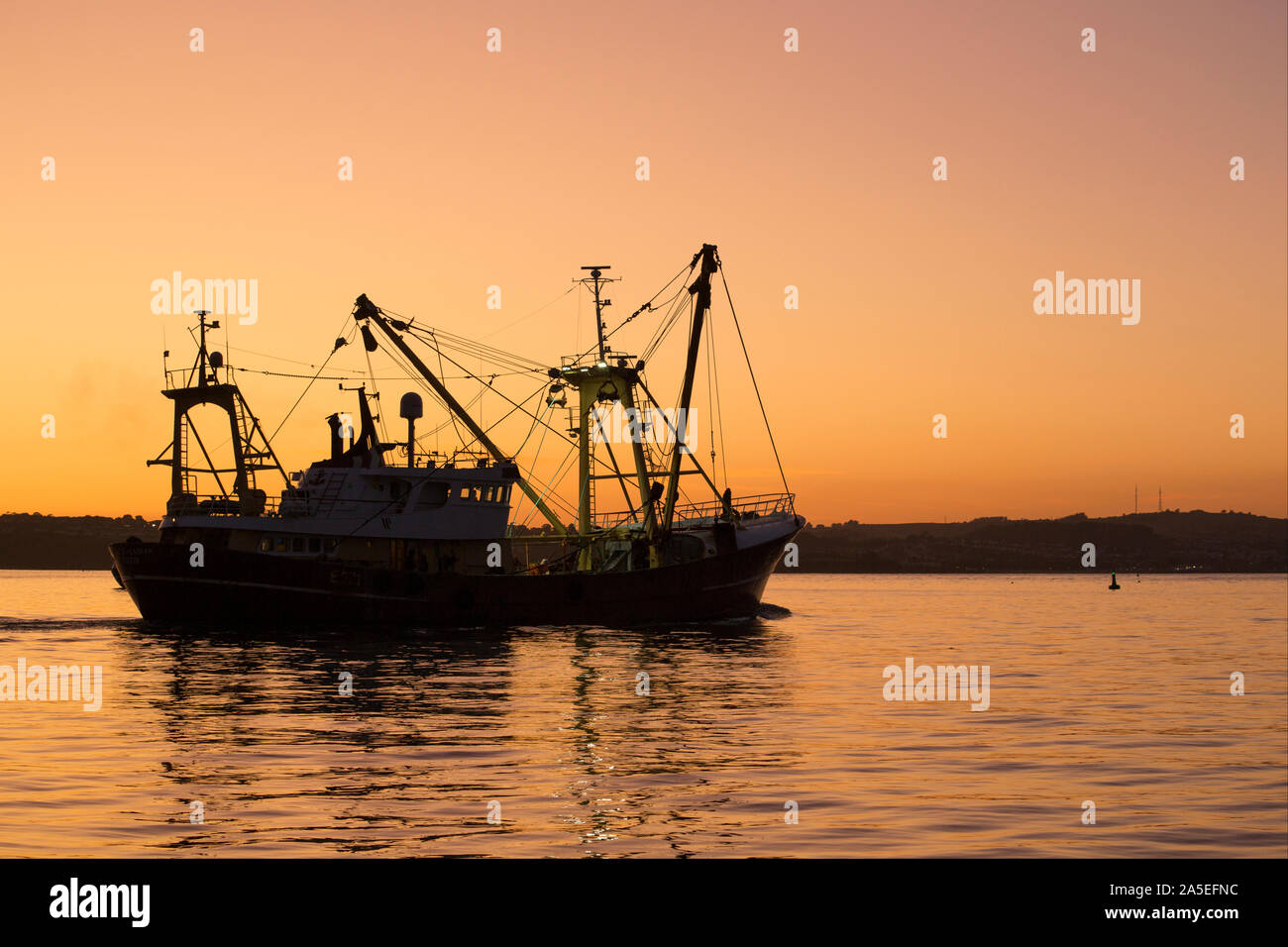 Ein Fischerboot verlassen Hafen von Brixham im Herbst, wenn die Sonne beginnt zu setzen. Brixham ist die Heimat einer großen Fischereiflotte und einen Fischmarkt. Devon Engla Stockfoto