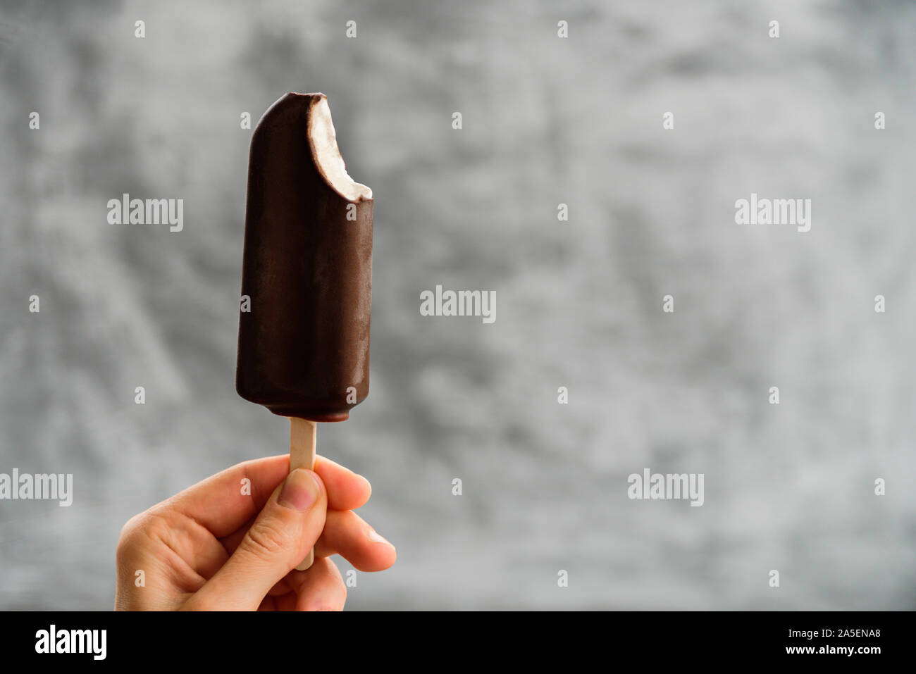 Woman Holding aus Eskimo Pie Eis in der Hand auf grauem Hintergrund gebissen. Eskimo Pie tag Konzept Stockfoto