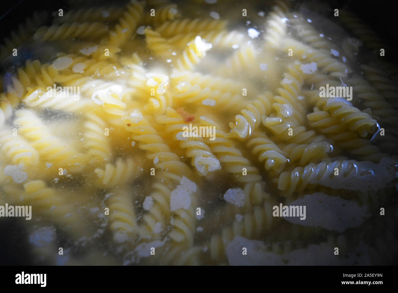 Home Kochen und Bereiten köstliche warme Gerichte. Der Prozess des Kochens spiralförmigen Teigwaren aus Hartweizen. Gelbe Nudeln in heißem Wasser in sonnigen Farben. Stockfoto