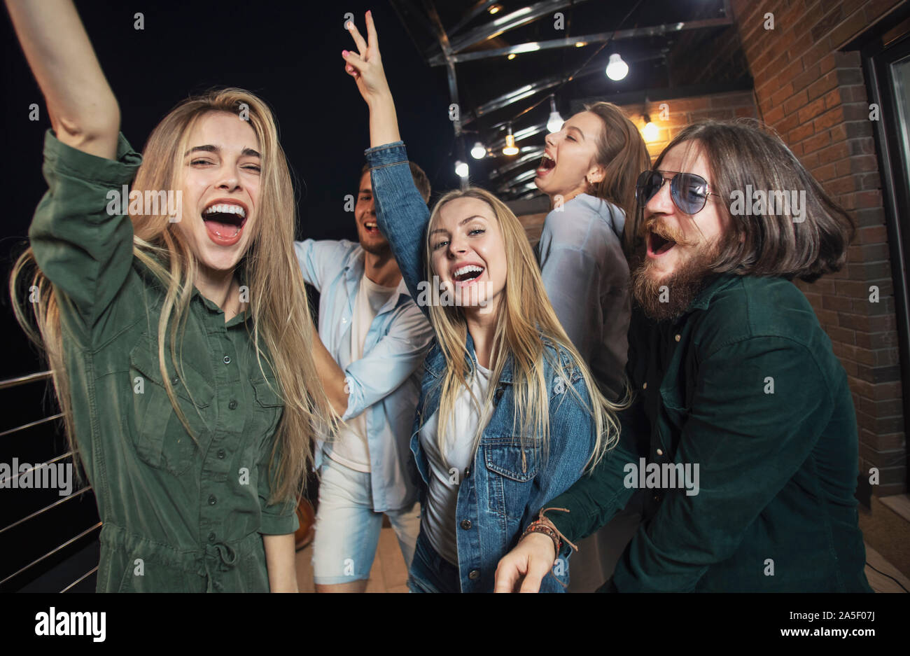 Fröhliche Freunde tanzen die ganze Nacht lang während ihrer Partei auf einem Dachboden Balkon Stockfoto