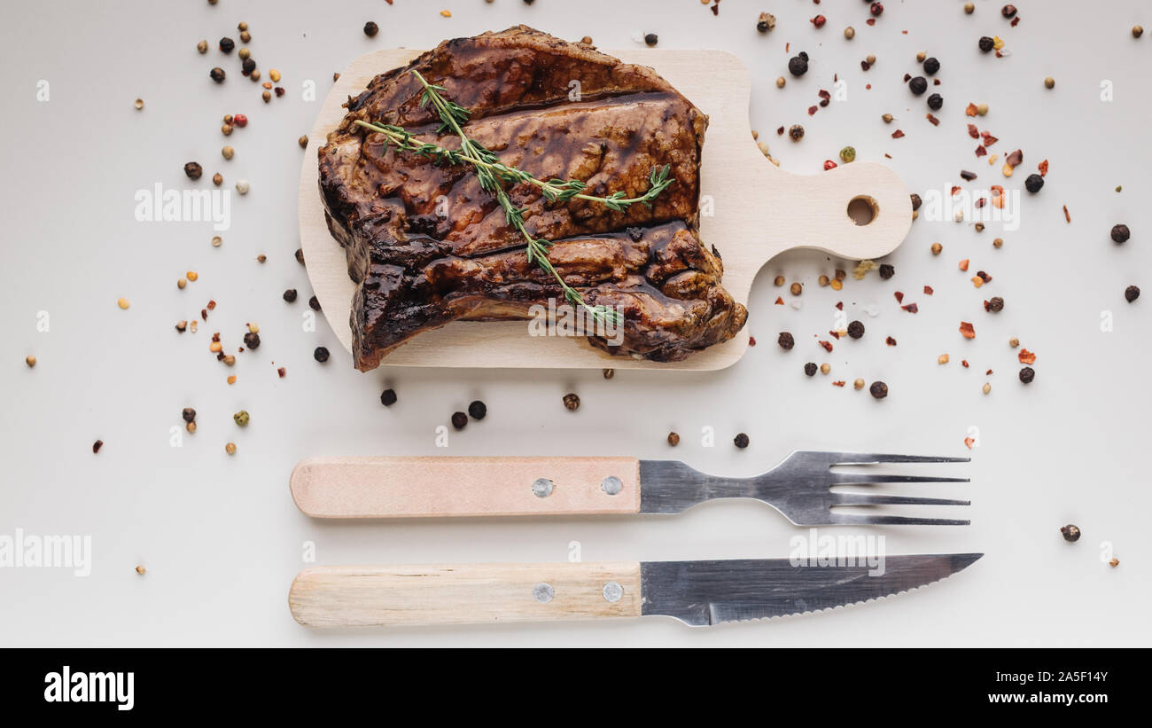 Appetitlich medium rar gegrillten T-Bone Steak auf einem hölzernen Schneidebrett auf hellem Hintergrund mit Gewürzen. Horizontale Schuß Stockfoto