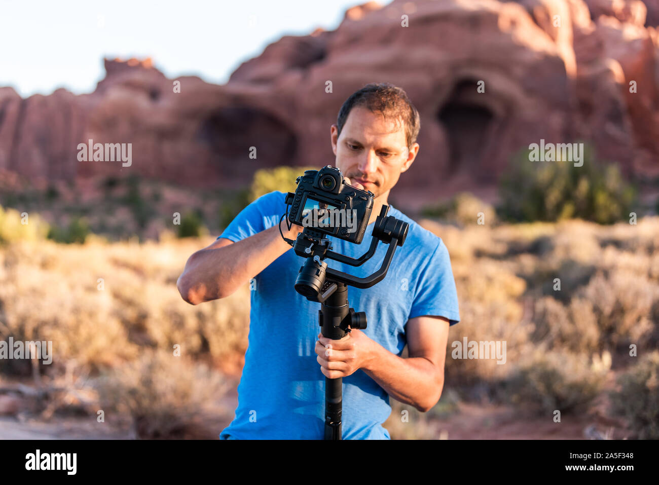 Double Arch Parkplatz im Arches Nationalpark in Utah beim morgendlichen Sonnenaufgang mit Mann Reinigung Kamera gimbal Stabilisator mit Anzeigen Stockfoto