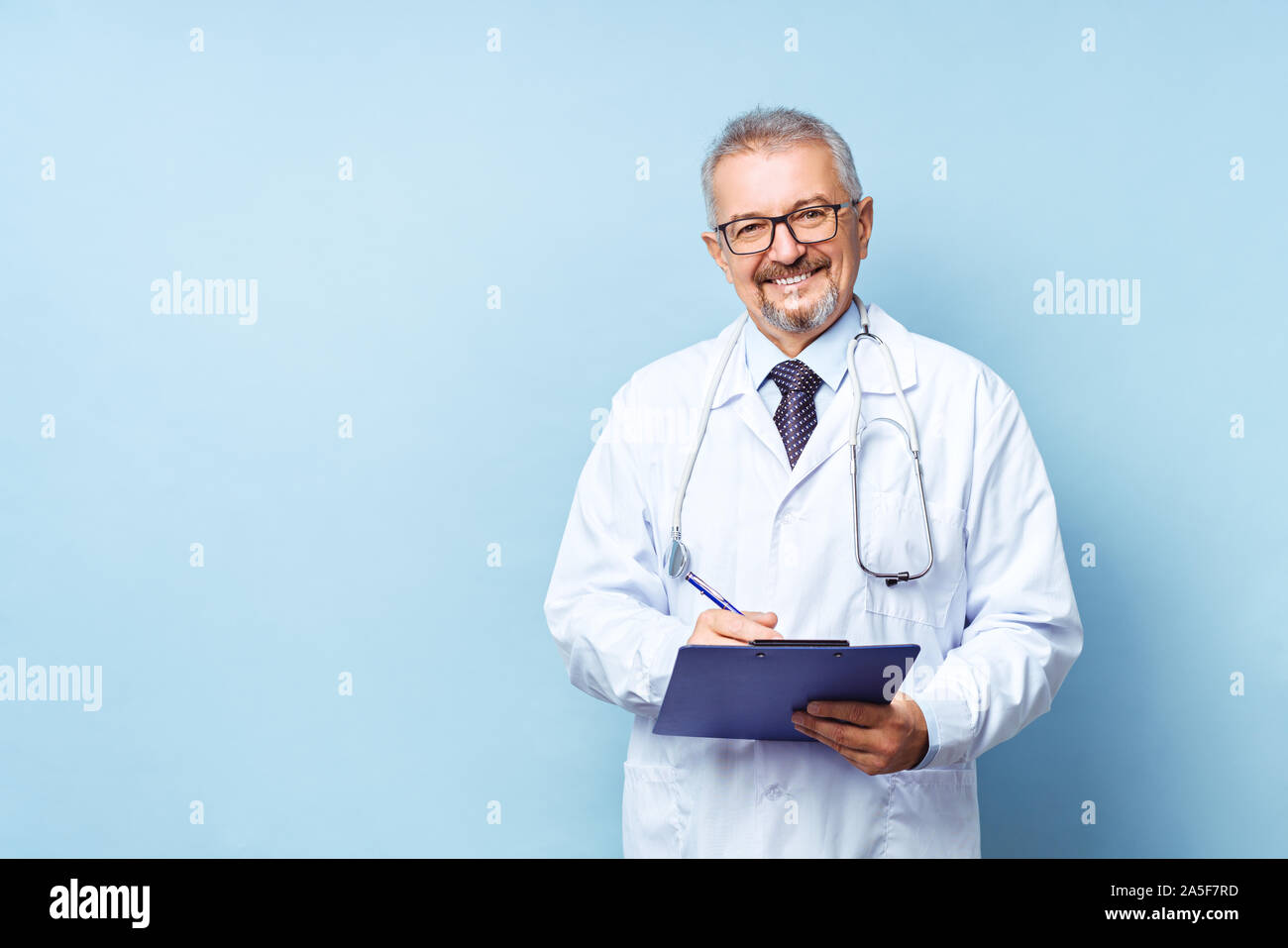 Lächelnd medizinische leitender Arzt mit einem Stethoskop. Auf einem blauen Hintergrund. Der Arzt hält die Ordner in der Hand und macht einen Termin in der Klinik Stockfoto