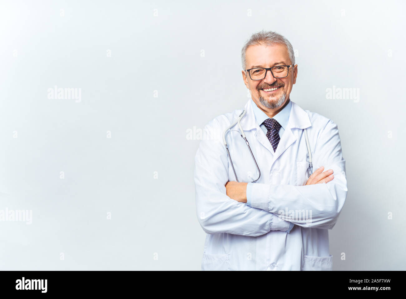 Fröhliche reife Arzt posing und lächelnd an Kamera, Gesundheitswesen und Medizin. Auf blauem Hintergrund isolieren. Stockfoto