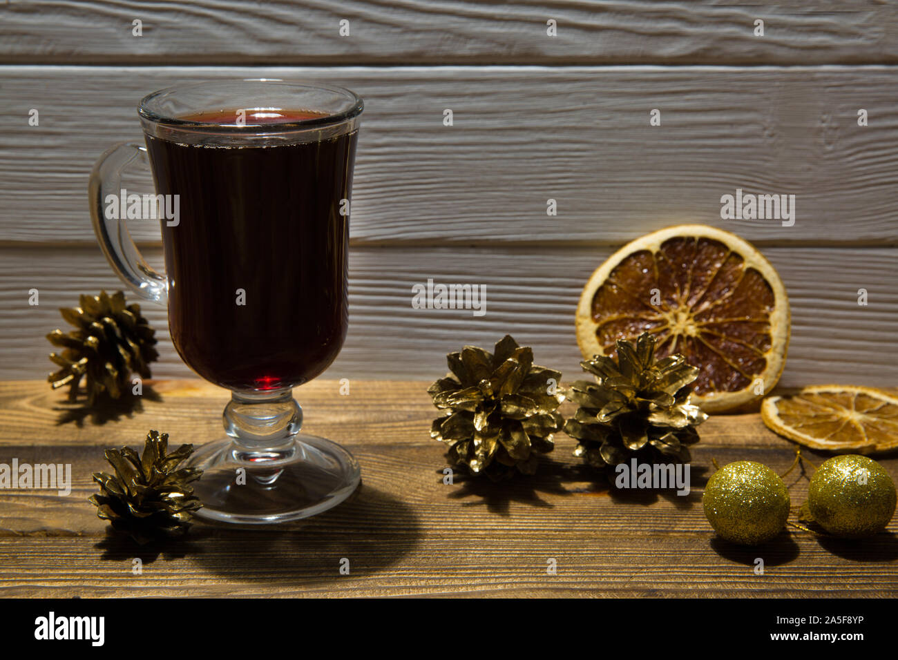 Rote Glühwein mit getrockneten sizilianischen Orangenscheiben Dekoration. Goldene Tannenzapfen und goldenen Kugeln. Braune Holztisch Hintergrund. Stockfoto